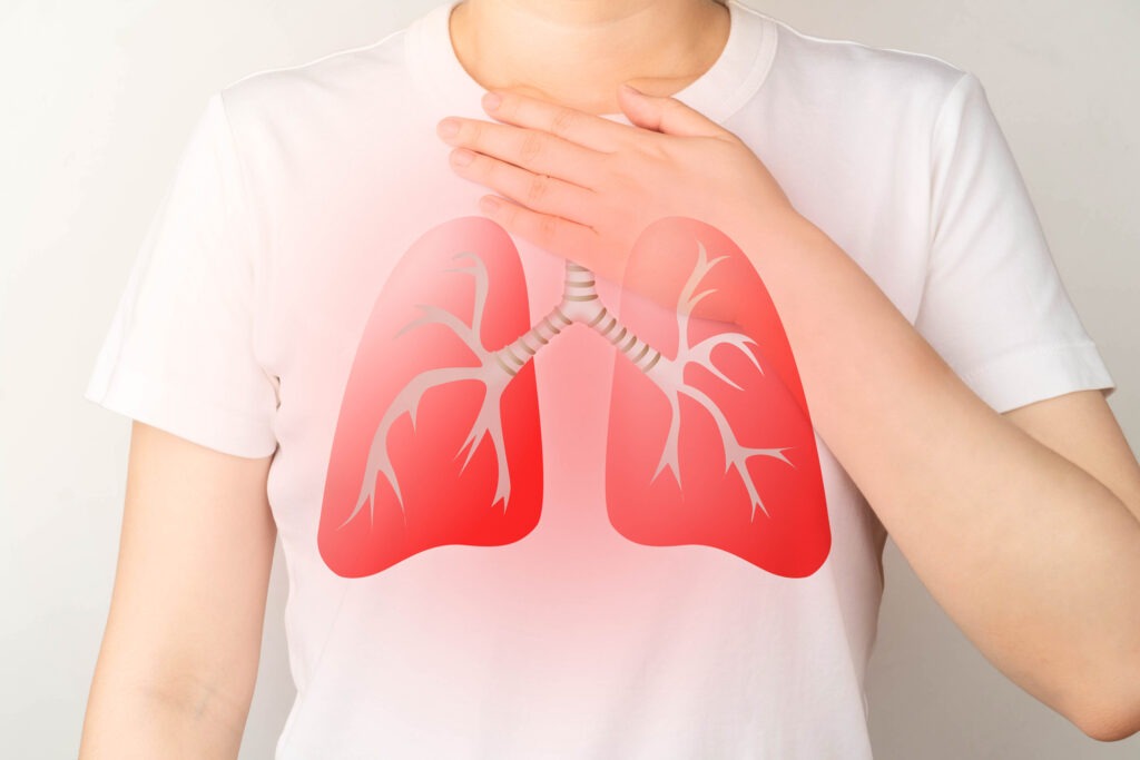 A person wearing a white t-shirt with a graphic of red lungs on it, holding their hand over their chest, emphasizing respiratory health.