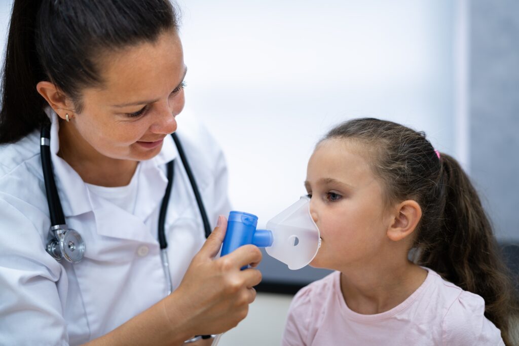 A healthcare professional administers therapy using a nebulizer mask to a young girl in a clinical setting, illustrating pediatric respiratory care.